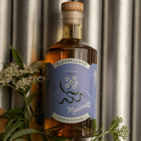 Bottle of Elderflower liqueur with a blue label against a metallic background